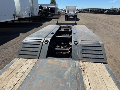 Trail King lowboy trailer deck with pony motor wells and heavy steel ramps, 50 ton capacity, center viewed from rear showing winches and mechanical components.