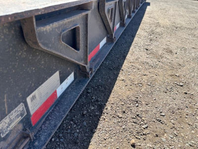 Lowboy trailer side view showing upper deck framework and reflective stripes along the edge.
