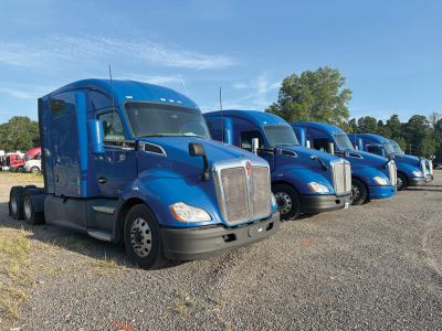 Kenworth T680 conventional day cab on lot showing blue exterior and row of trucks.