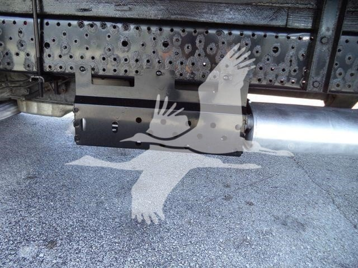 Underbody view of isuzu NPR-HD truck showing a cylindrical fuel tank and metal frame with perforated side panels; watermark of two birds overlapping.