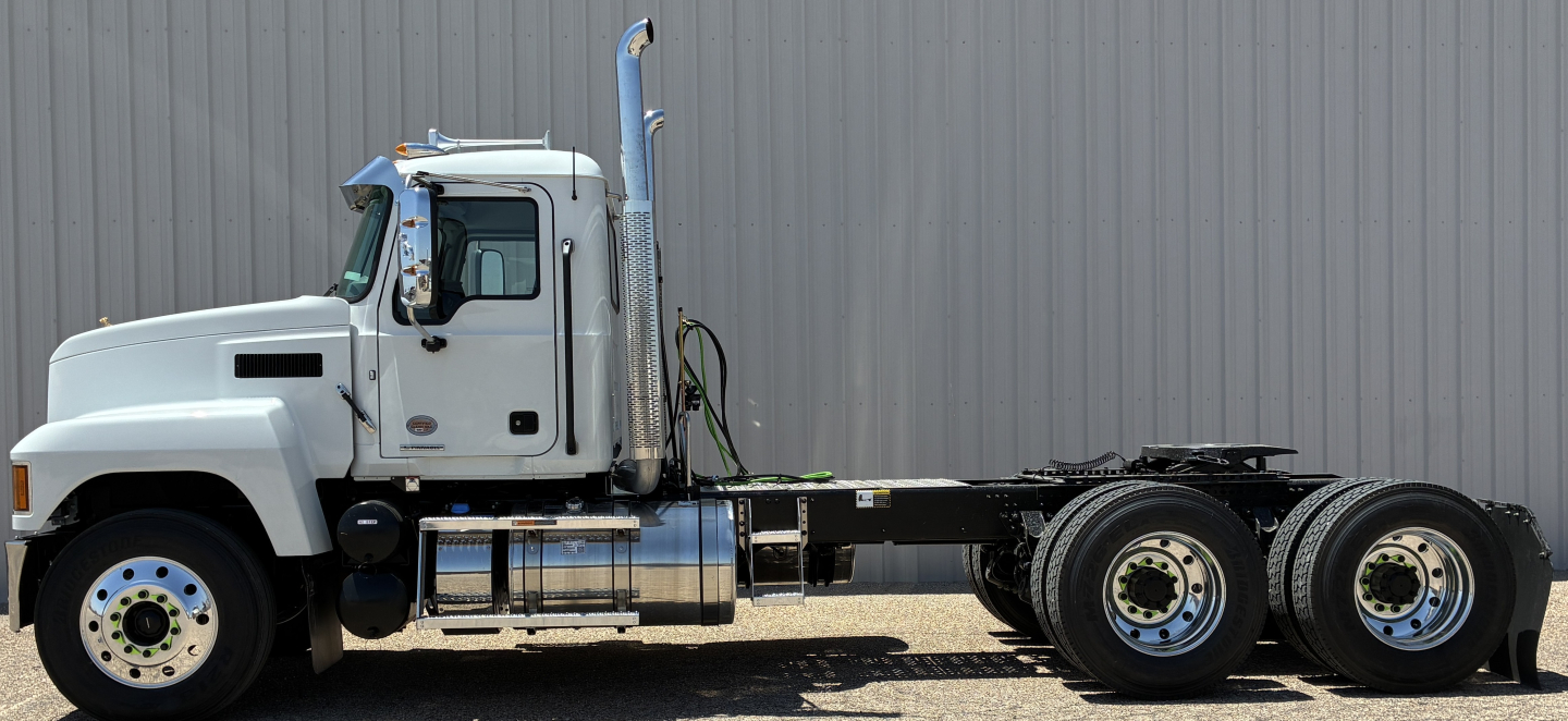 Truck chassis side view showing 3-axle configuration and diesel fuel tanks. Mack PI64T conventional daycab with white cab and black frame, VIN plate area not legible.