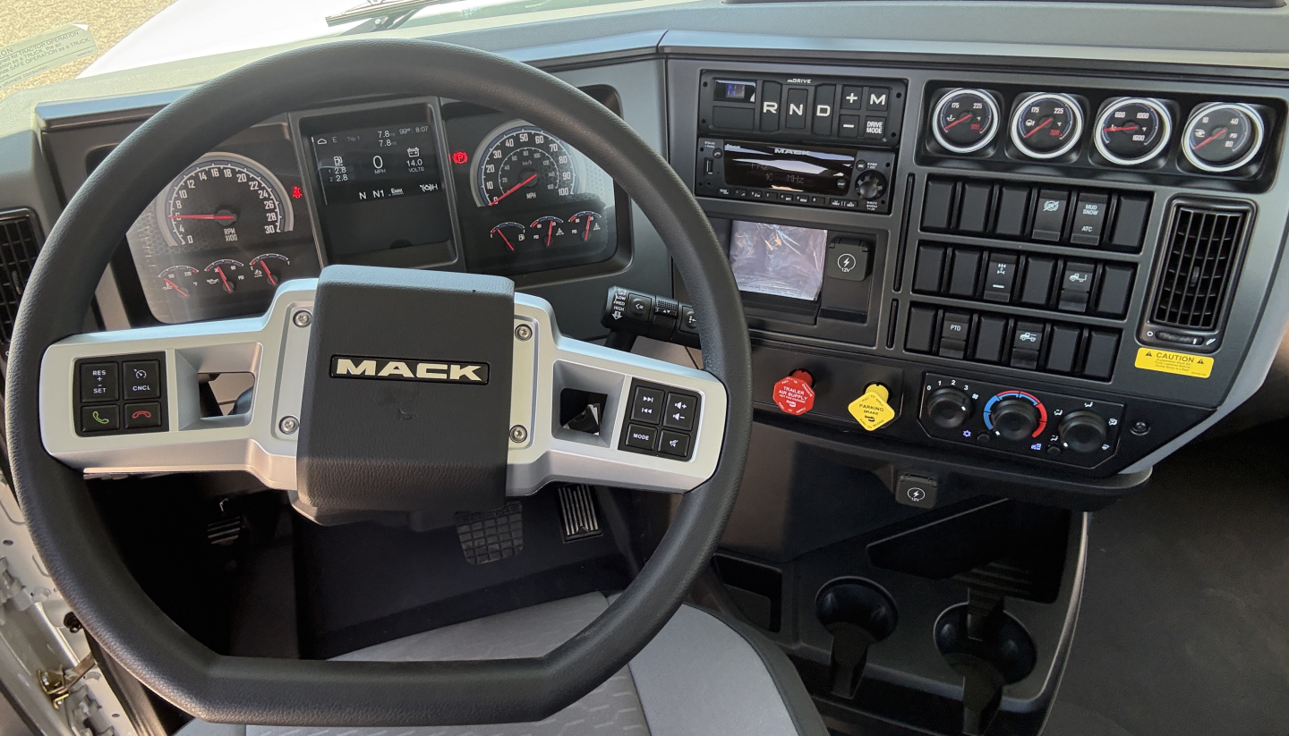 Mack PI64T truck cockpit showing steering wheel and dash gauges with controls.