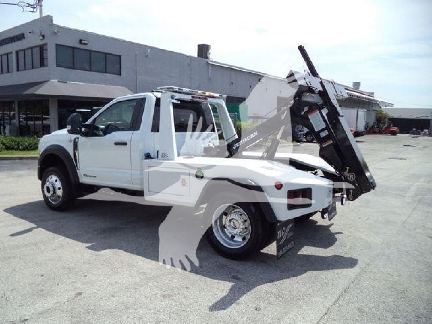 Ford F-450 tow truck with a hydraulic bed tilt in a parking lot, white cab, and black riser; side view showing front and rear tires and winch bed.