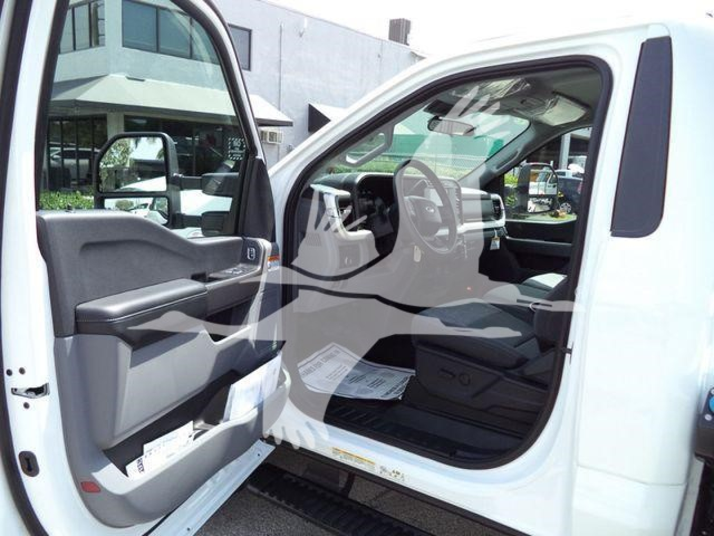 Truck interior: open driver-side door showing steering wheel, dashboard, and front seat of a white Ford F-450 with a visible side mirror.