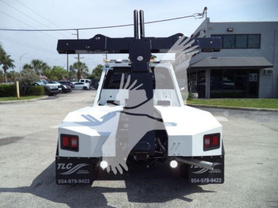 Rear view of a white Ford F-450 utility truck with a large black winch crane arm mounted behind cab, rectangular taillights, and TLC branding on mud flaps; stock number J40065FM visible.