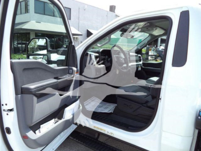 Truck interior: open driver-side door showing steering wheel, dashboard, and front seat of a white Ford F-450 with a visible side mirror.