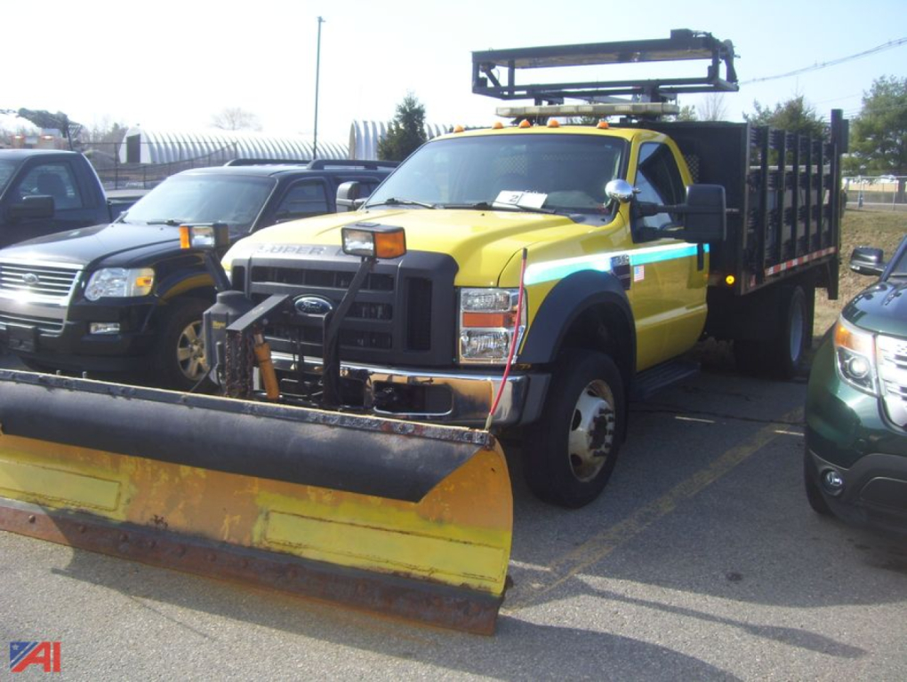Ford F-550 Super Duty stake truck with plow and yellow cab, black stake bed, and front-mounted snow plow blade.