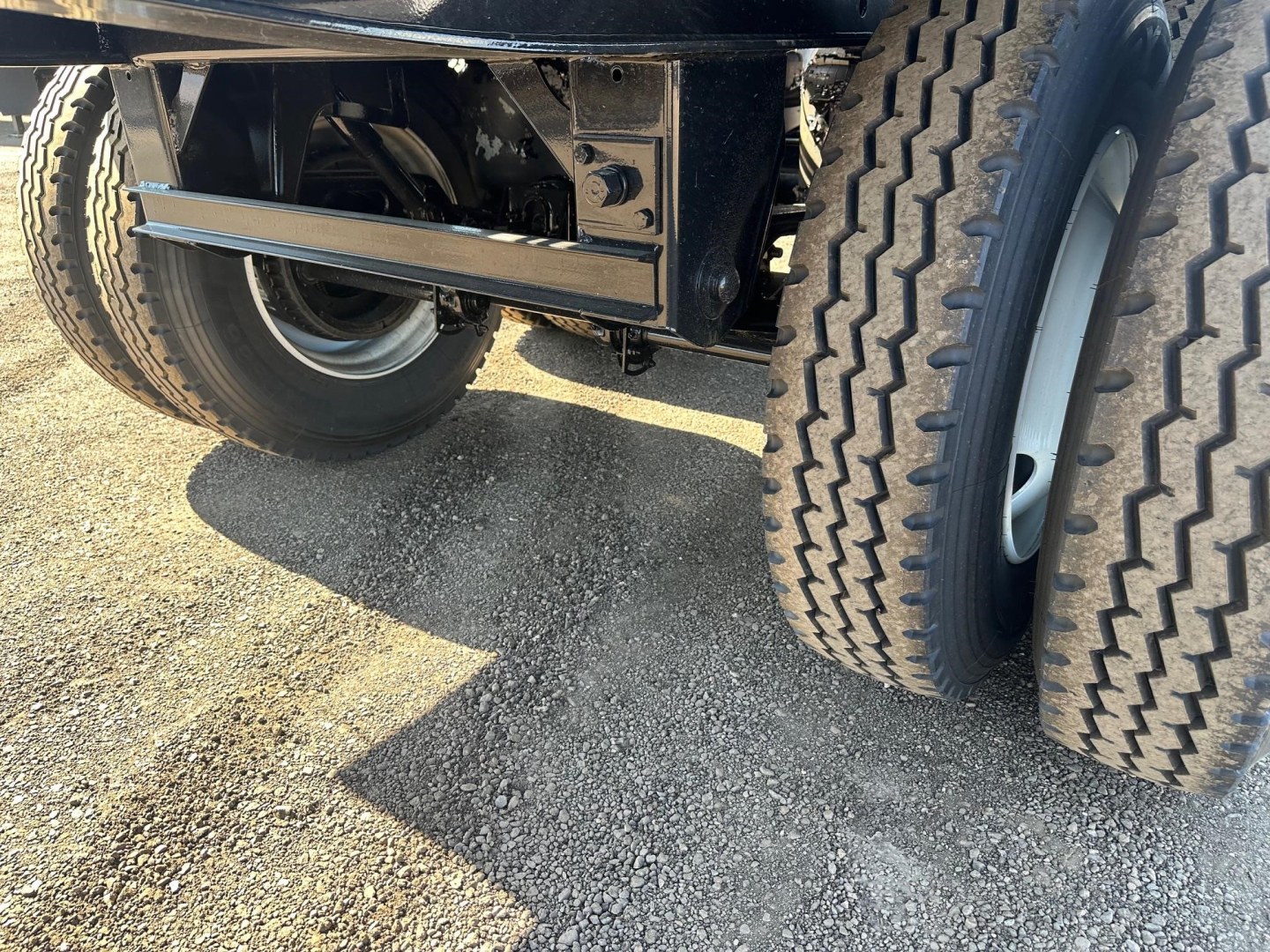 Truck trailer undercarriage showing dual rear axles with large off-road tires and suspension components.