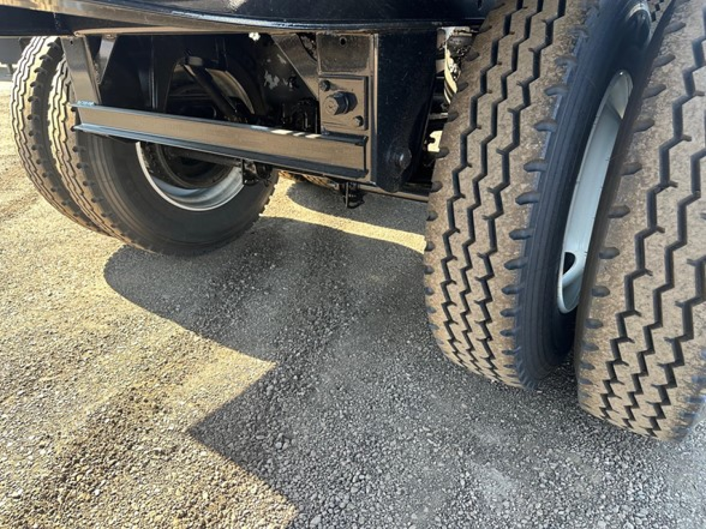 Truck trailer undercarriage with dual rear axles and tires, metal frame, suspension components visible.