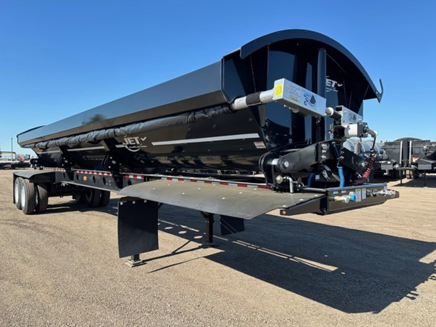 Trailer with large black tank and dual axles, pivot points per side, tub flex corners, left side near support legs and control mechanisms visible.