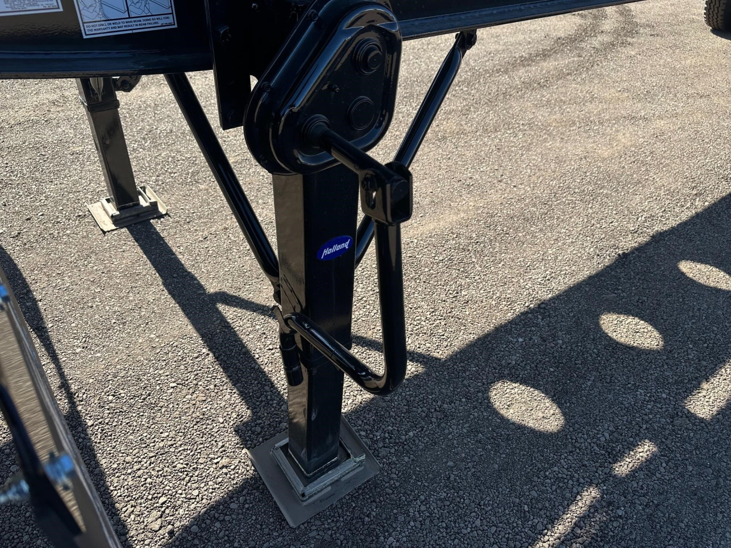 Trailer landing gear and front frame showing adjustable leg with pivot points and tube corners, black metal with a silver foot plate and small blue logo.