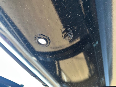 Trailer component showing a bolt and hole surface with black painted metal; hardware detail and riveted area visible.