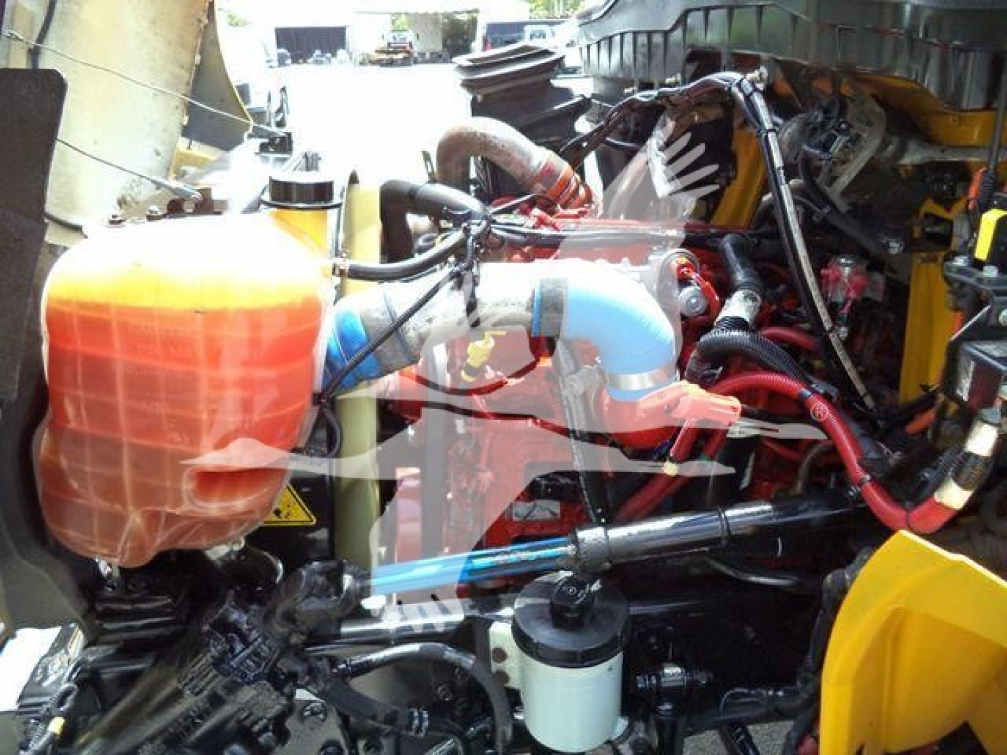 Truck engine bay of a 2019 International 4300 grapple truck showing coolant reservoir, hoses, and hydraulic lines.
