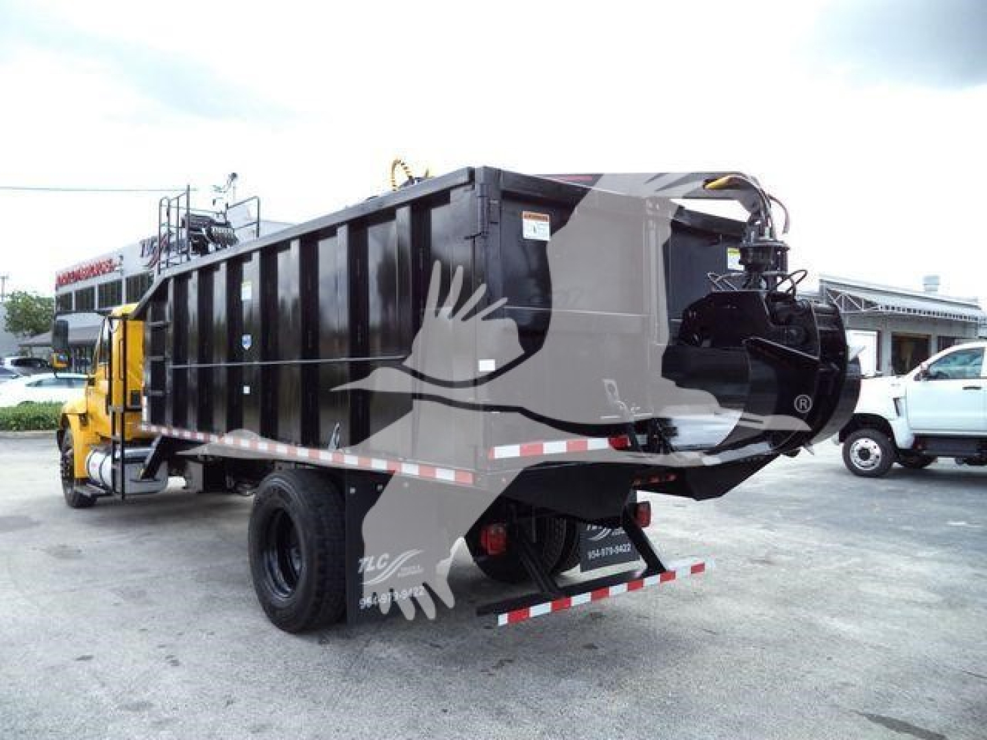 Truck side and rear with grapple truck body and dump bed, International 4300 style, black dump container, rear hitch and taillights visible.
