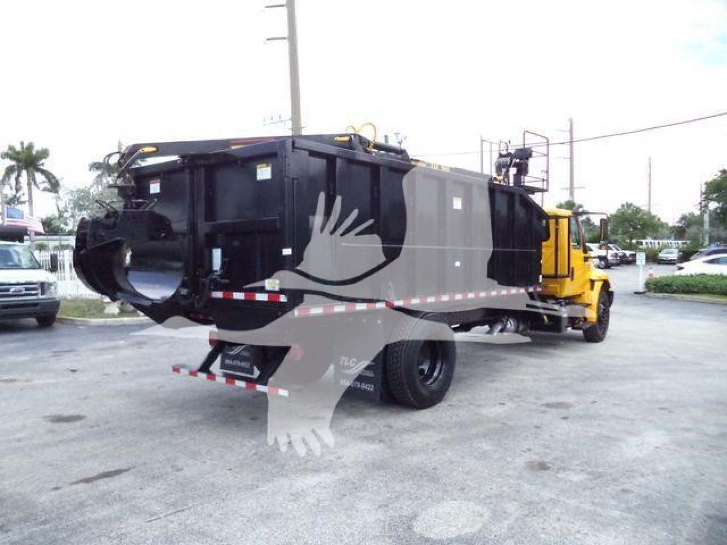 Dump truck/grapple truck with black bed and yellow cab, rear view showing side panels with riveted seams and a license plate area; no legible text visible.