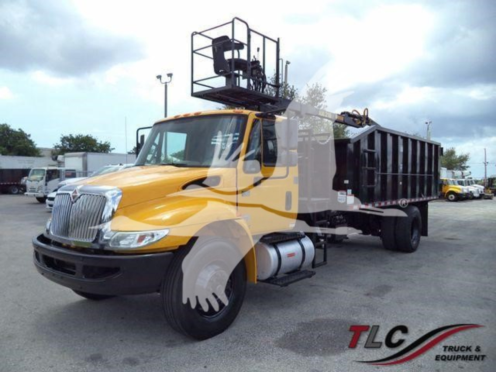 Truck with grapple hook and raised platform on dump bed showing International 4300 front view and equipment top lift arm in yard.