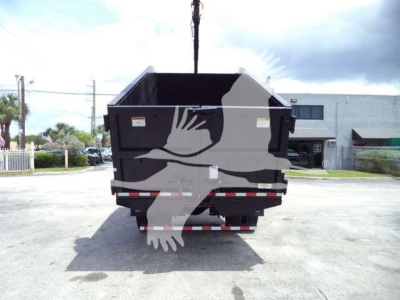 Back view of a dump truck bed on a hook, with a crane hook above. T83650FM stock label not visible on bed. Wide concrete lot.