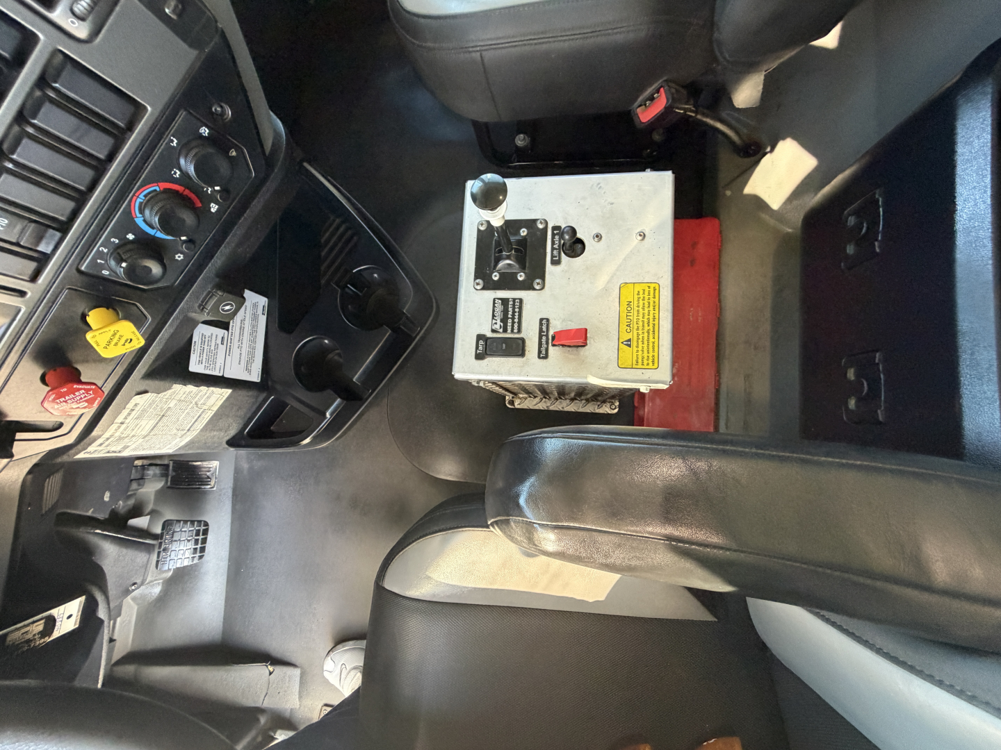 Cab interior of a 2024 Mack GR64F dump truck showing driver seat, center console, steering area, and a metal controller box with labels and switches.