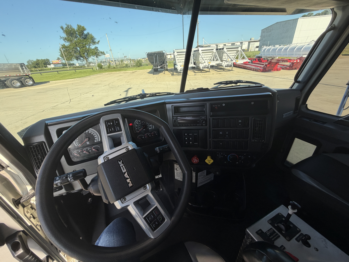 Cab interior of a 2024 Mack GR64F dump truck showing steering wheel with Mack logo, dashboard gauges, and control panel.