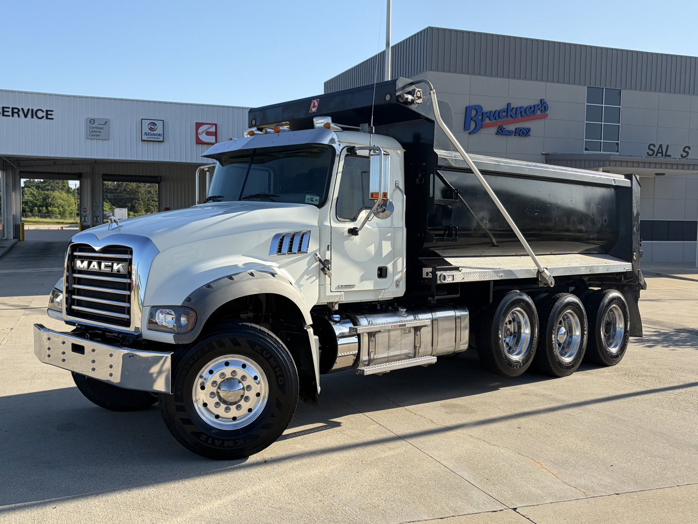 Mack GR64F dump truck with black dump body and white cab, side view showing chrome bumper, dual rear axles, and hoist mechanism.