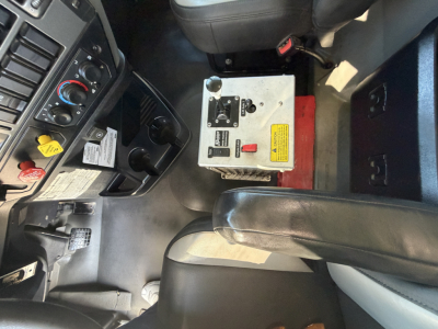 Cab interior of a 2024 Mack GR64F dump truck showing driver seat, center console, steering area, and a metal controller box with labels and switches.