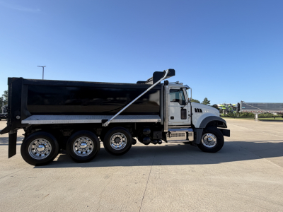 Dump truck side view showing Mack GR64F with large black dump bed and chrome wheels in a parking lot.