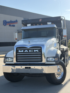 Mack GR64F dump truck front-facing view showing chrome grille with MACK lettering, dual headlights, large bumper, and dump bed in background.