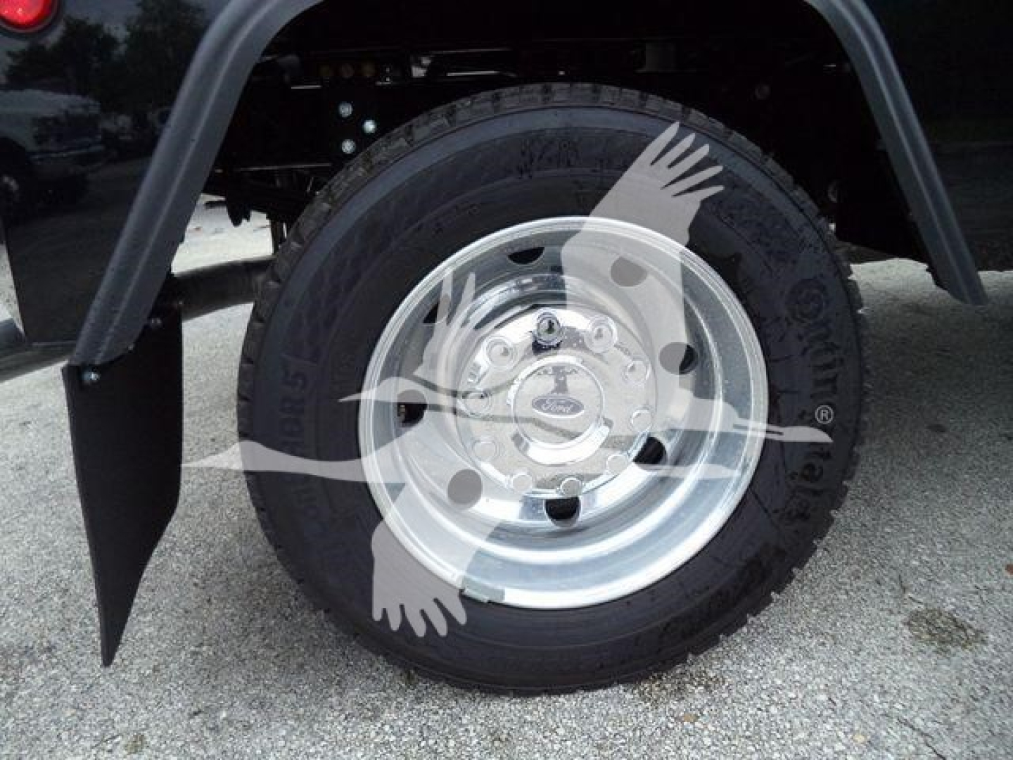 Wheel assembly and tire on a Ford F-450 truck with mud flaps and chrome wheel; partial fender and undercarriage visible.