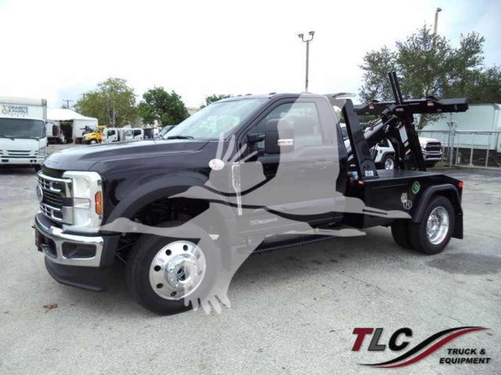 Ford F-450 Tow Truck with a wheel-lift bed, dark cab, and front chrome grille, side view showing stake bed and equipment; dealer watermark.