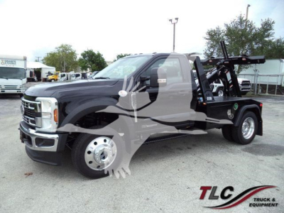 Ford F-450 Tow Truck with a wheel-lift bed, dark cab, and front chrome grille, side view showing stake bed and equipment; dealer watermark.