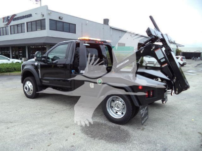 Truck with a winch bed and a hydraulic hooklift system, branding on the side reads 'Jerr-Dan' with a black color and ceiling lights on cab.