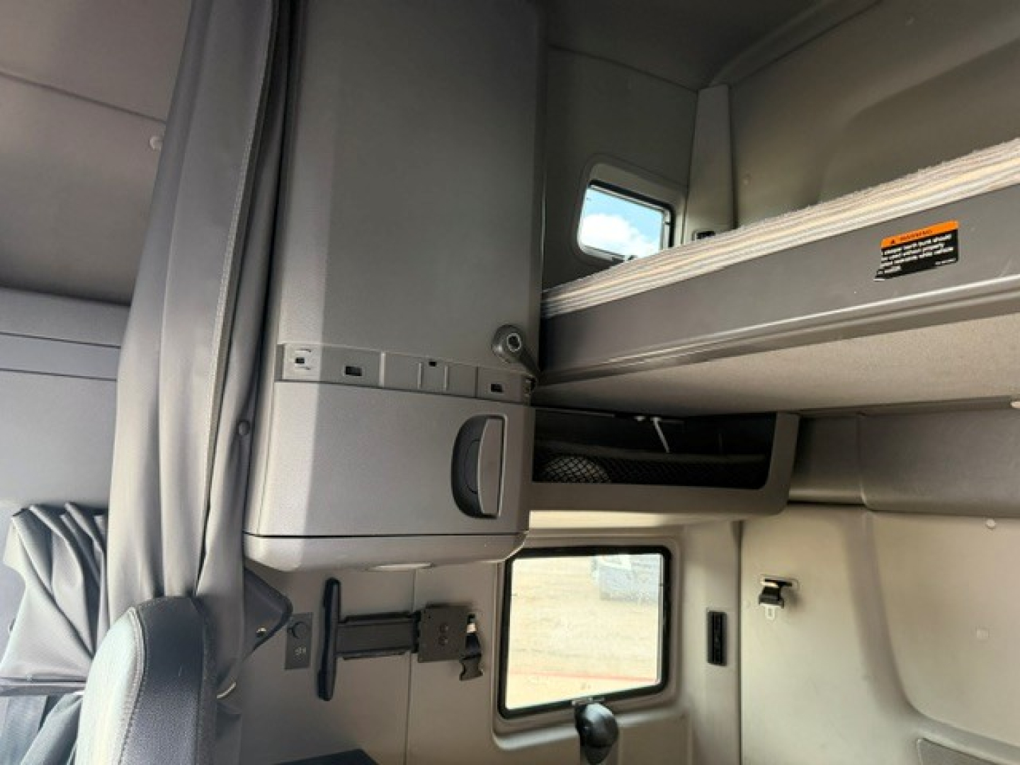Interior sleeper cab of a 2022 International LT showing storage compartments, overhead bunk, window, and control panels.