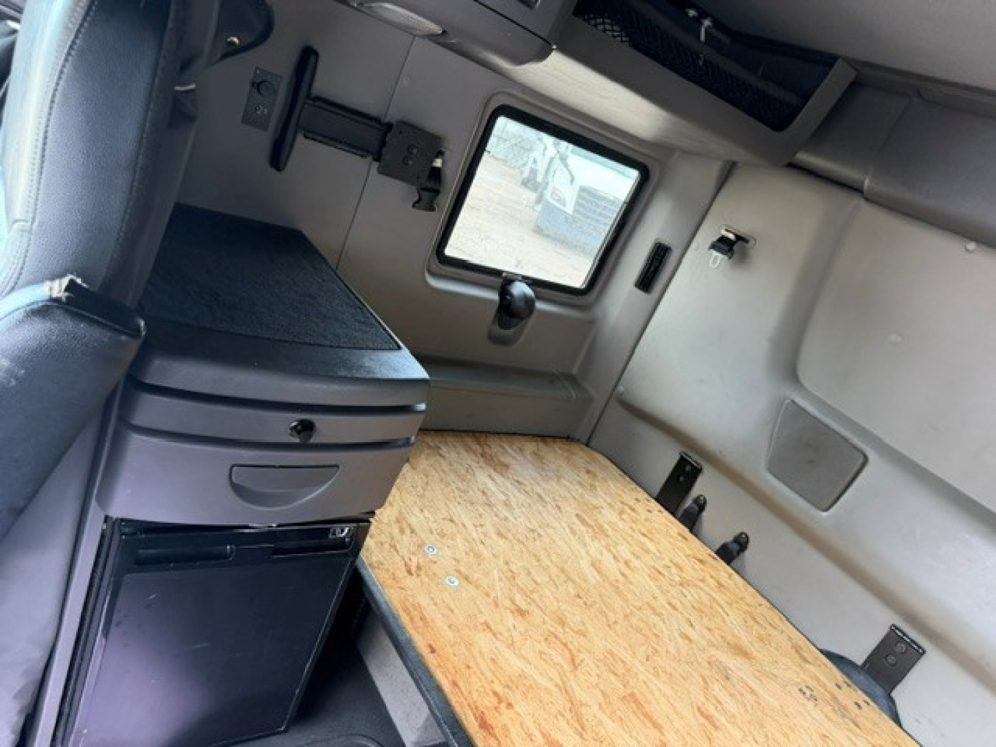 Truck sleeper cab interior with wooden table top, storage drawers, window, and mounting hardware visible.