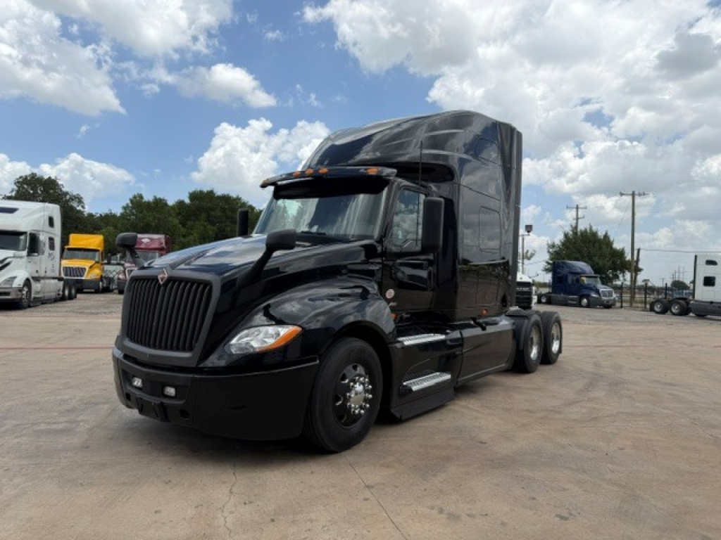 Truck cab on a black 2022 International LT sleeper tractor, angled front view with tall sleeper, daytime sky, other trucks in background.