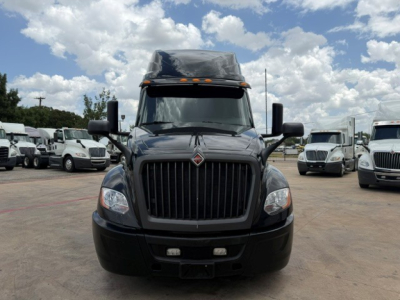 Front view of a 2022 International LT truck in a dealership lot. Black grille with International emblem, large bumper, side mirrors, and sleeper cab visibility. Other trucks in background.