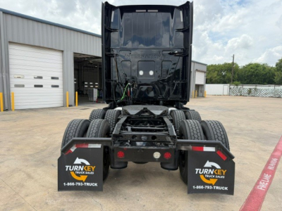 Tractor-trailer cab seen from rear showing fifth-wheel and dual rear axles, black truck frame, Turnkey Truck Sales mud flaps, and dealership lot.