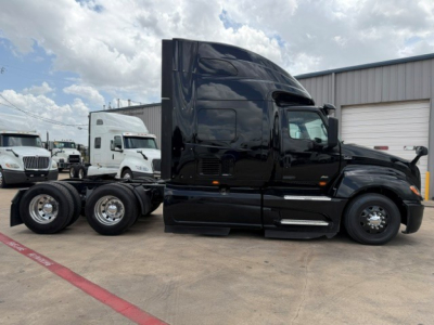 Truck cab and chassis of a black 2022 International LT, side view. Curved sleeper cab with high roof. Visible wheels and tandem axle. Reflection on glossy paint.