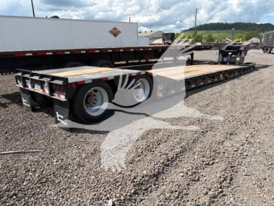 Lowboy trailer showing long flatbed with dual rear axles and white wheels. Visible are wheel wells, trailer deck, and rear bumper lights.