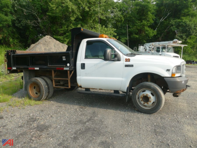 2004 Ford F-450 Super Duty dump truck side view with white cab and black dump bed, dual rear wheels, on gravel lot.