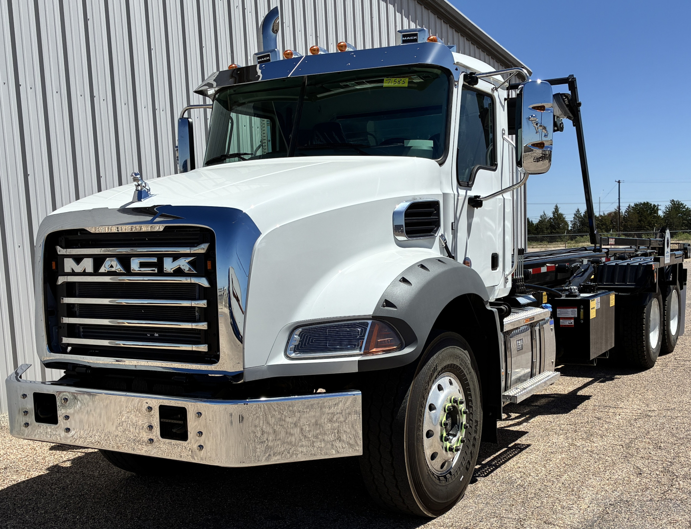 Mack GR64B truck in white cab with chrome front bumper and grille, side mirrors, and long hauler bed; windshield with slight blue tint and blue rooftop lights.
