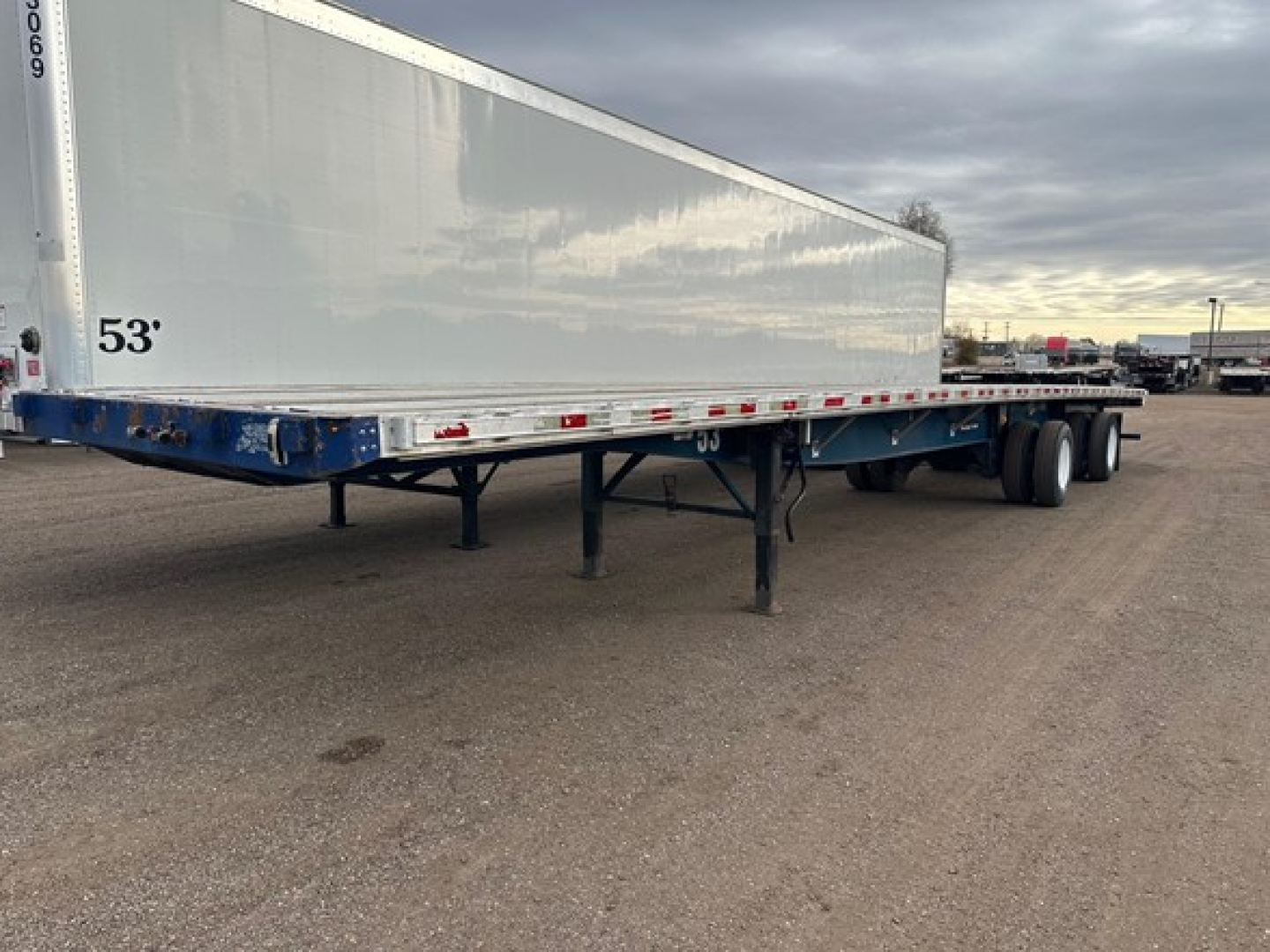 Flatbed trailer showing side with 53' trailer length marking and blue undercarriage fittings.