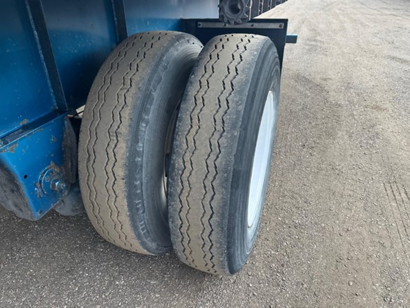 Dual rear trailer tires on a 2014 Great Dane Freedom LT flatbed trailer, view of left side with blue frame and gravel surface.