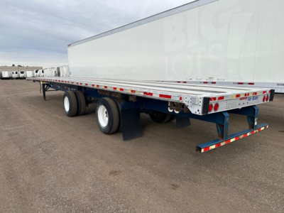 Flatbed trailer showing dual rear axles and trailer frame with reflective tape and BigTech branding on the side.