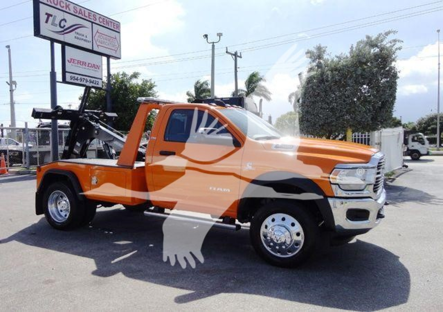 Tow rig with orange Ram 4500 pickup truck and winch equipment mounted in bed, side view showing front grille, dual rear wheels, and dealership signage in background.