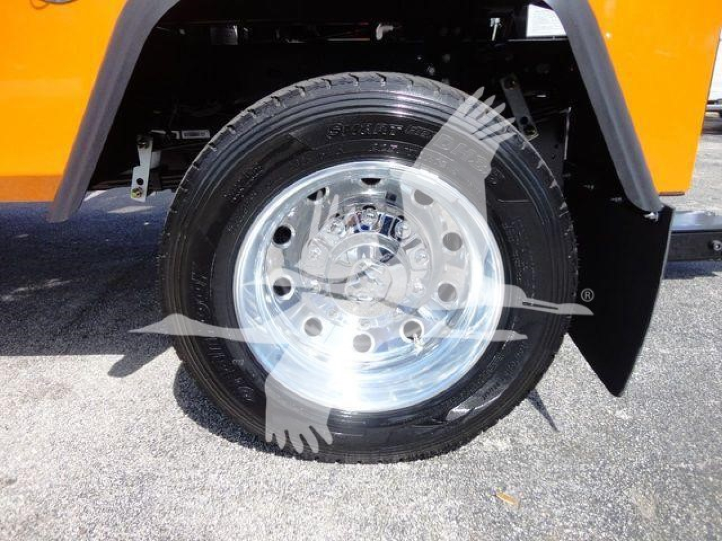 Truck wheel close-up showing a mounted black tire with a shiny polished rim on an orange Ram 4500 SLT, front fender area and black mudflap visible.