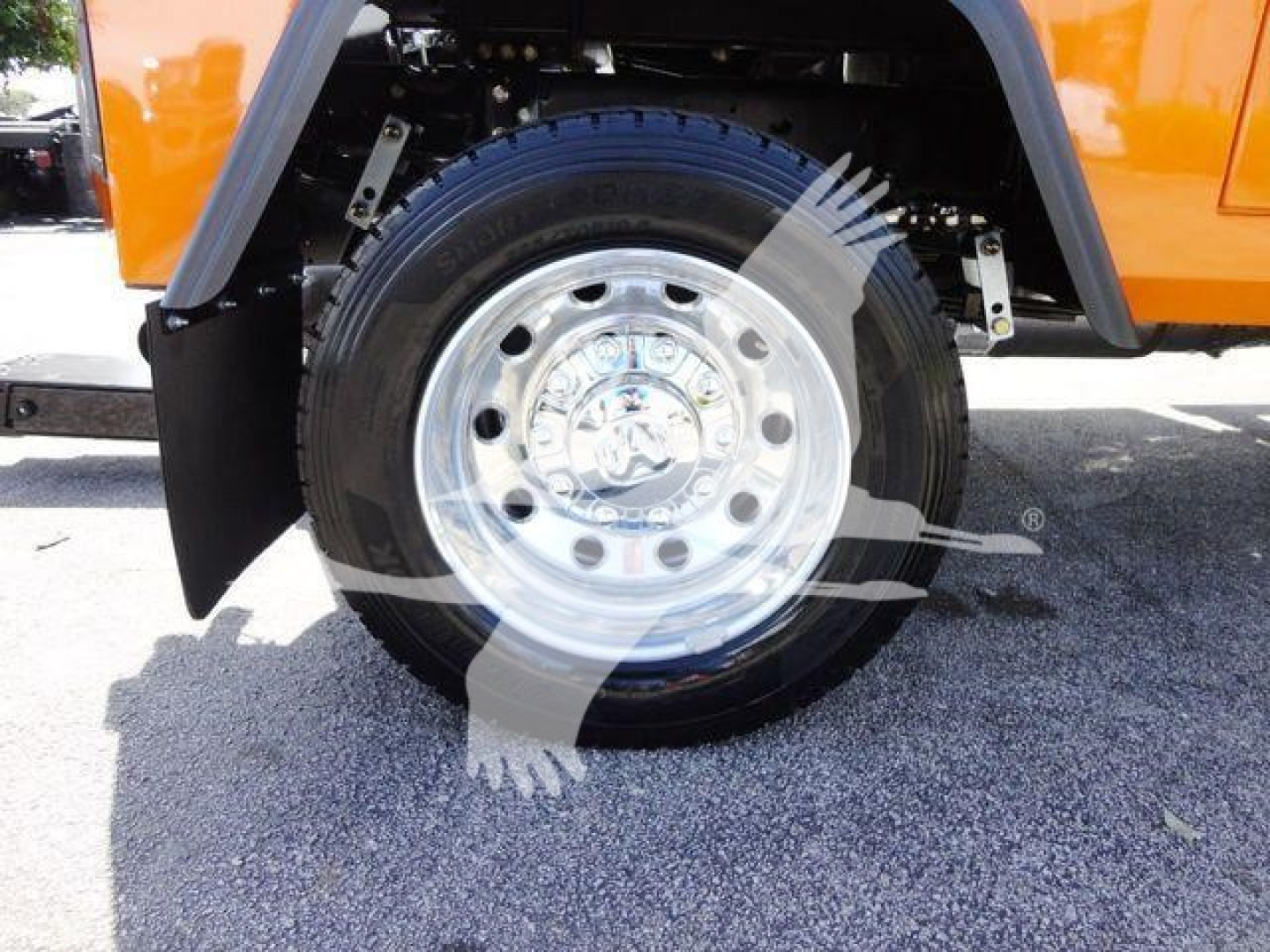 Wheel and hub of a bright orange Ram 4500 truck showing polished chrome wheel and tire, front fender near suspension components.