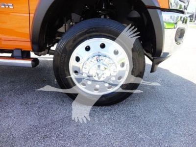 Front wheel of a 2024 Ram 4500 SLT on a bright orange truck; chrome hubcap, black tire, visible suspension components and fender; partial view of the truck side.