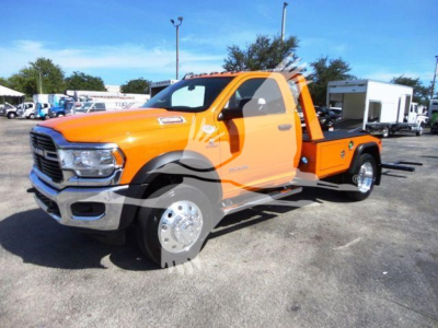 Orange 2024 Ram 4500 SLT tow truck/flatbed in a dealership lot, side view showing cab and rear flatbed with chrome wheels.