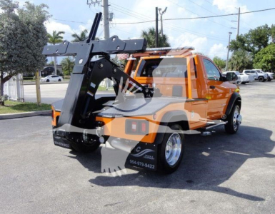 Tow truck or utility truck with mounted winch attachment and lifting arm, orange cab, black chassis, rear winch assembly visible.