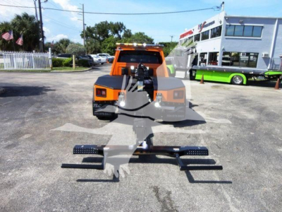 Ram 4500 winch truck in orange cab with front-mounted heavy-duty winch and black skid bar assembly on the ground; dealership building in background.